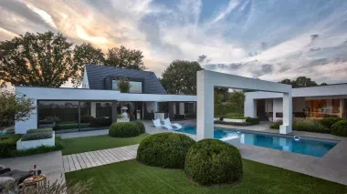 Onderhoudsvriendelijke tuin met strak gazon, haagwolken en een houten loper die doorloopt tot het poolhouse.