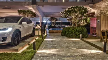 Showtuin Knops Tuindesign met spots verlicht kasseienpad naar plungepool, links Schellevis-tegels in groene border, als plateau voor luxe auto.